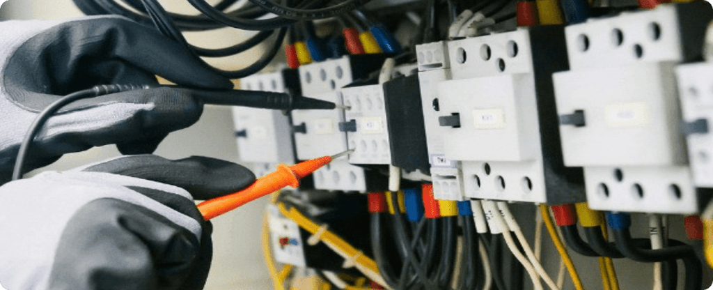 Professional electrical contractor performing diagnostic testing on a complex electrical control panel with colorful wiring.