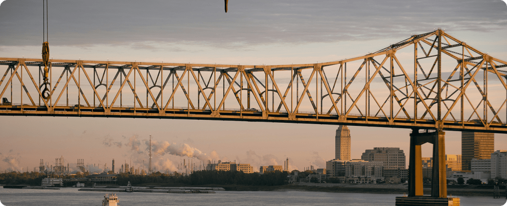 Large-scale infrastructure and industrial construction project in Louisiana, featuring a steel bridge and heavy machinery near a riverfront.