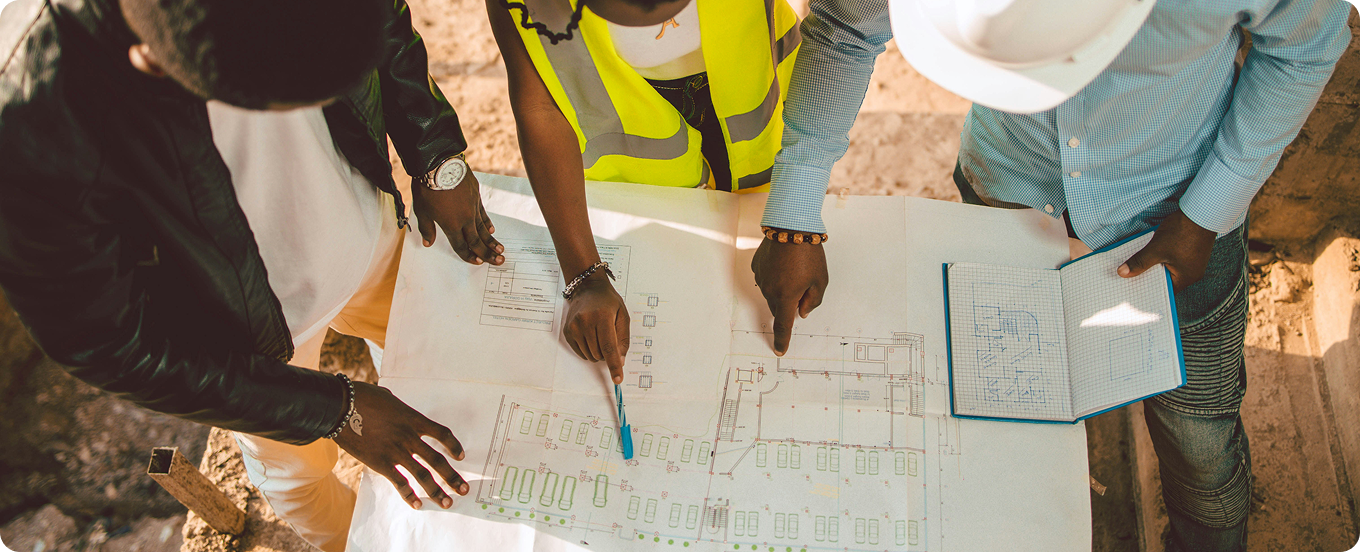 A qualifying agent and construction team conducting a site plan review and discussing project responsibilities over technical blueprints.