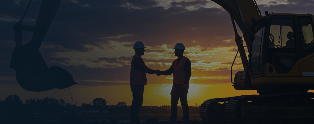 General contractor and client shaking hands on a construction project site with heavy machinery and excavators in the background.