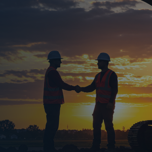 General contractor and client shaking hands on a construction project site with heavy machinery and excavators in the background.